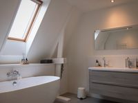 Badkamer onder schuin dak met dakraam waaronder ligbad en badkamermeubel