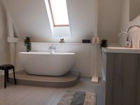 Badkamer op zolder met dakraam waaronder een bad op plateau